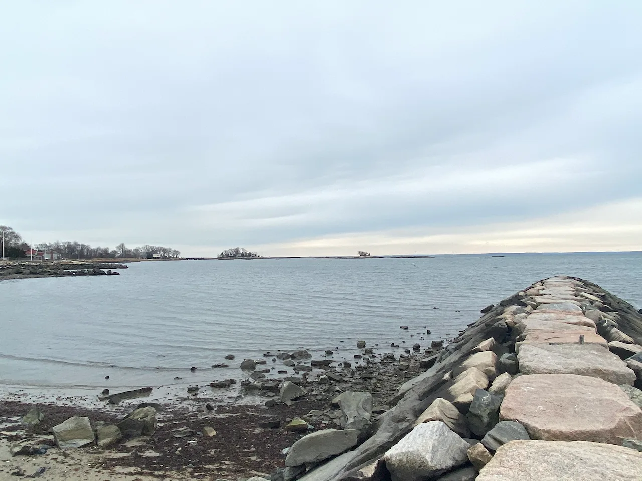 Looking back across Westcott Cove toward Vincent Island, with a stone jetty extending into the water from the foreground.